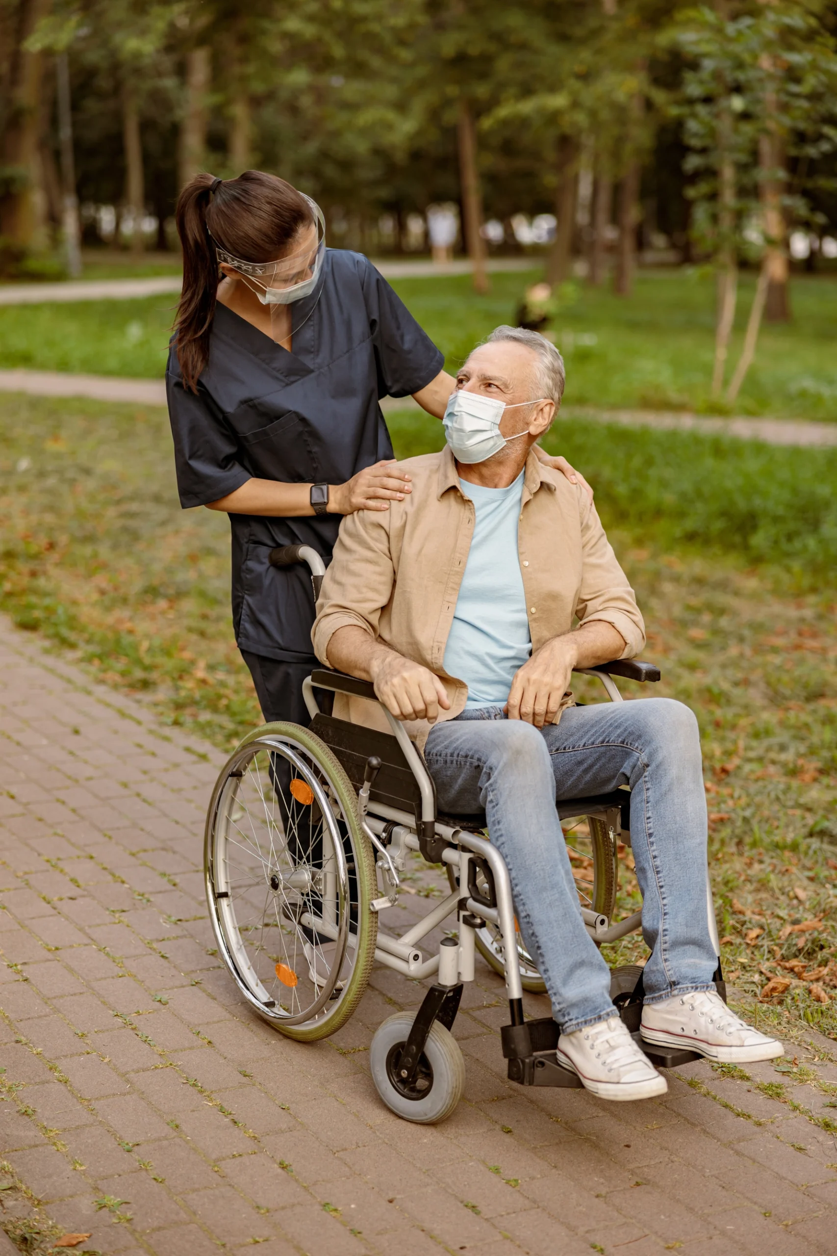 kind caregiver talks with man in wheelchair and medical mask